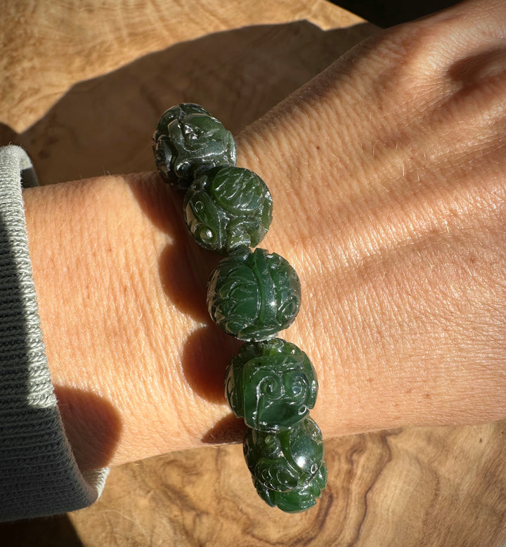 A beaded bracelet made of carved dark green jade-like round beads, displayed on a textured wooden surface. on someones wrist 