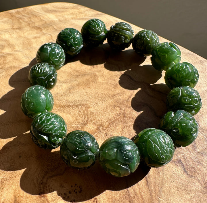 A beaded bracelet made of carved green jade-like round beads, displayed on a wooden surface.