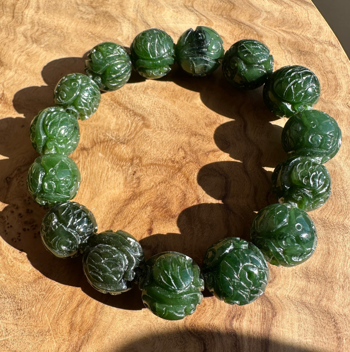 A beaded bracelet made of carved dark green jade-like round beads, displayed on a textured wooden surface.
