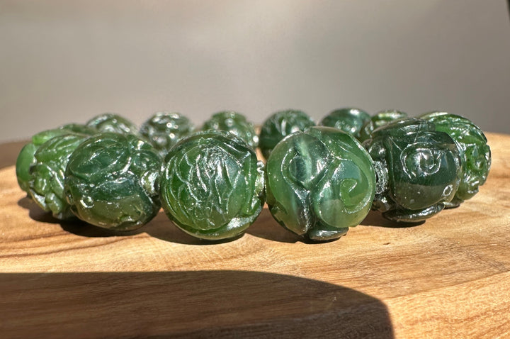A beaded bracelet made of carved dark green jade-like round beads, displayed on a textured wooden surface.