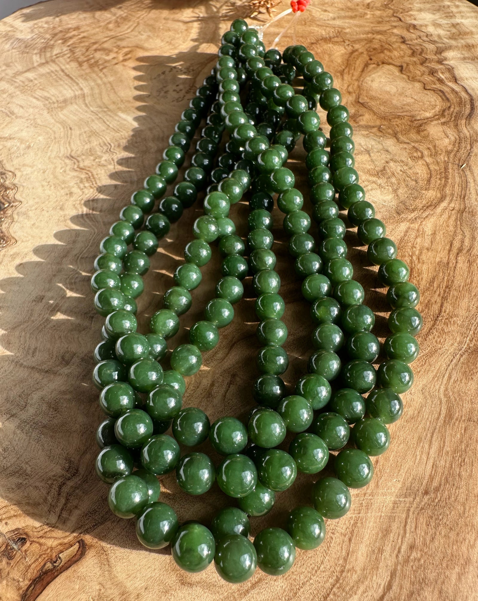 8mm dark green Canadian beads unstrung, multiple strands arranged on wood