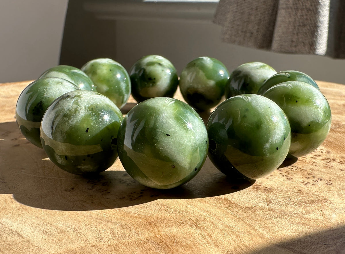 A set of polished green jade beads with natural white and dark green marbling, arranged in a circle on a light wood surface.