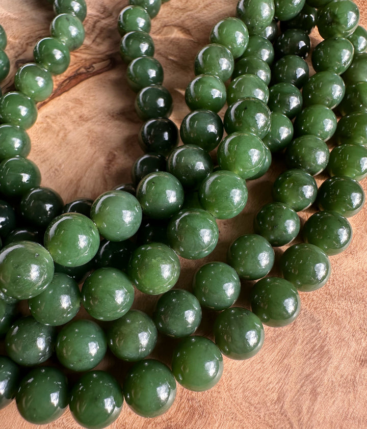 Dark green 8mm Canadian unstrung beads in loose strands on a wood surface