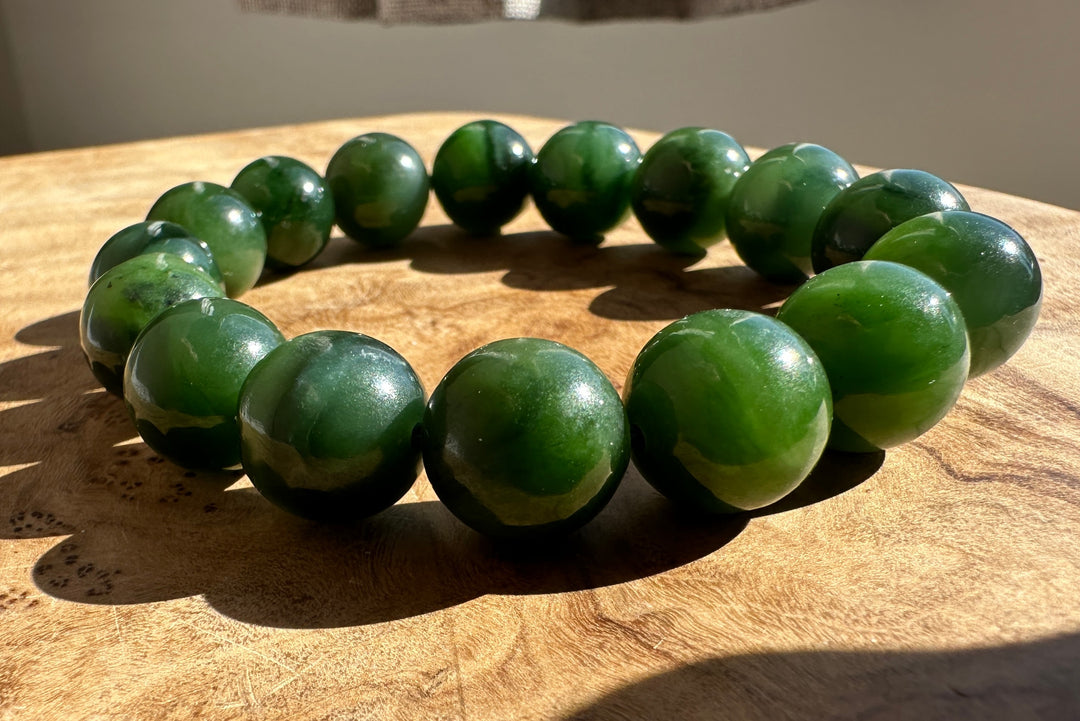A beaded bracelet made of glossy dark green polished stone beads, arranged in a circle on a wooden surface.