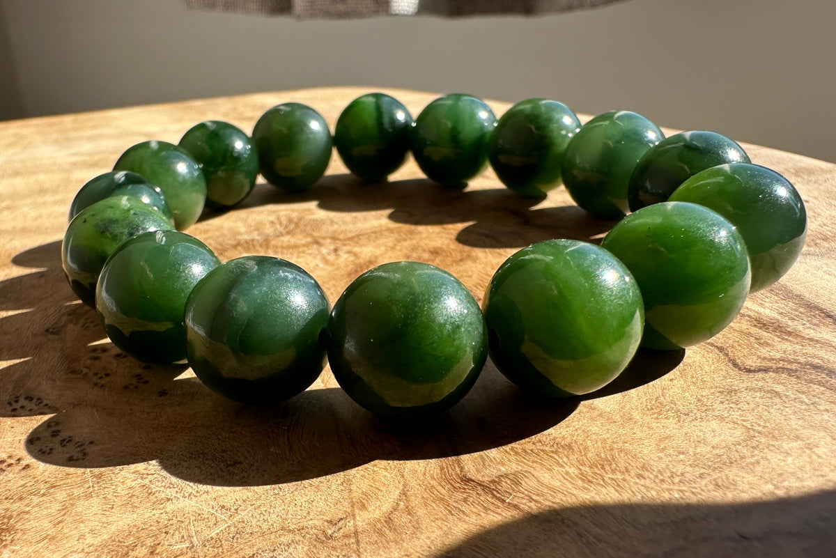 A beaded bracelet made of glossy dark green polished stone beads, arranged in a circle on a wooden surface.
