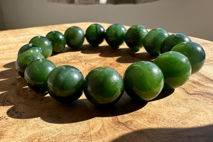 A beaded bracelet made of glossy dark green polished stone beads, arranged in a circle on a wooden surface.