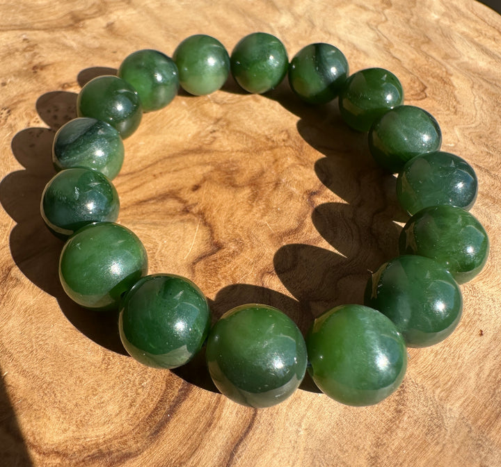 A beaded bracelet made of polished green stone beads arranged in a circle on a wooden surface.