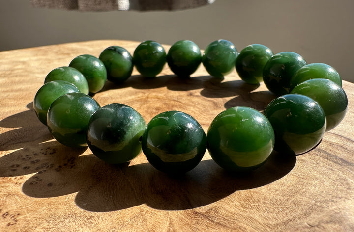A beaded bracelet made of glossy, polished green jade-like round beads, displayed on a rustic wooden surface.