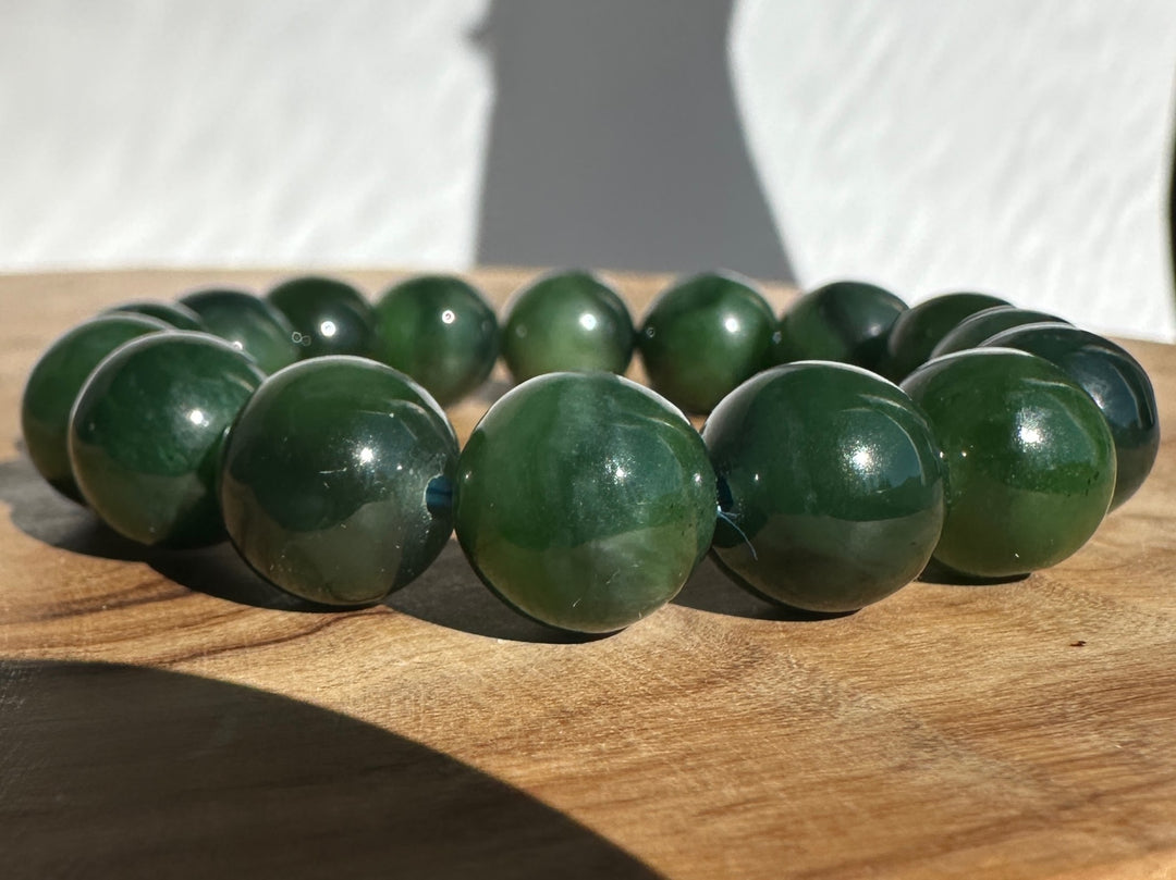 A beaded stretch bracelet made of glossy dark green round beads, resting on a wooden surface with a white textured background.