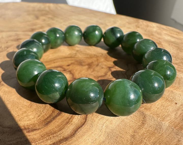 A beaded bracelet made of polished dark green jade-like round beads, displayed on a rustic wooden surface.