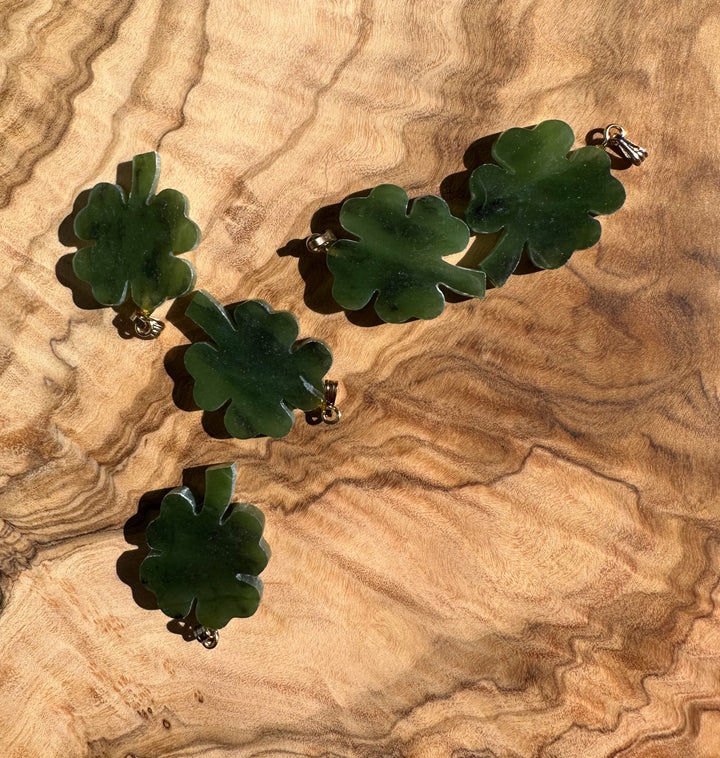 Multiple jade four leaf clover pendants displayed on a wood grain surface