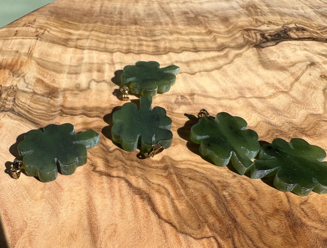 Group of vintage jade four leaf clover pendants with gold bails on wood