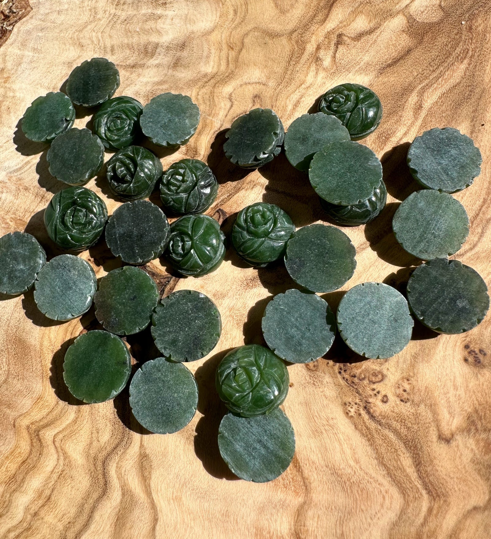 Assorted vintage dark green jade rose cabochons and round discs on a wooden surface