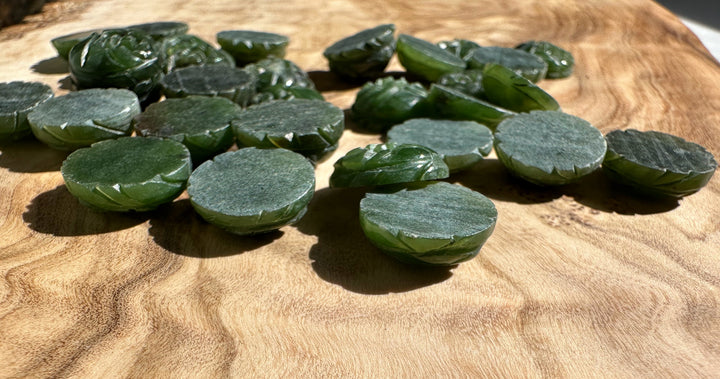 Close up of dark green jade rose cabochons and flat discs on a wood surface