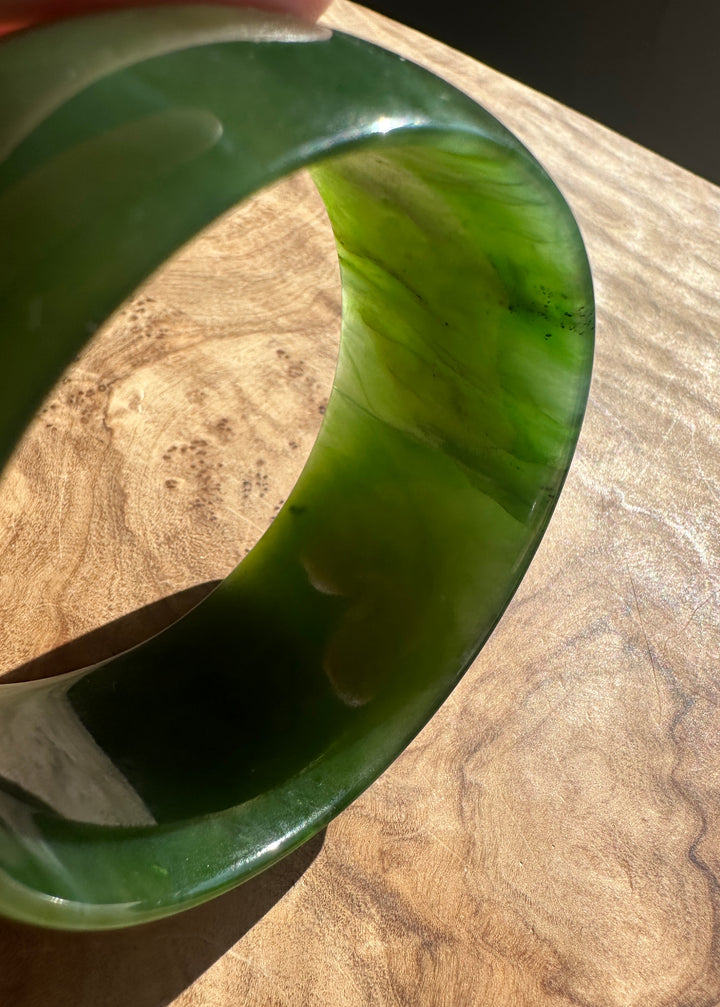A green jade bangle bracelet with natural marbling, resting on a wooden surface.