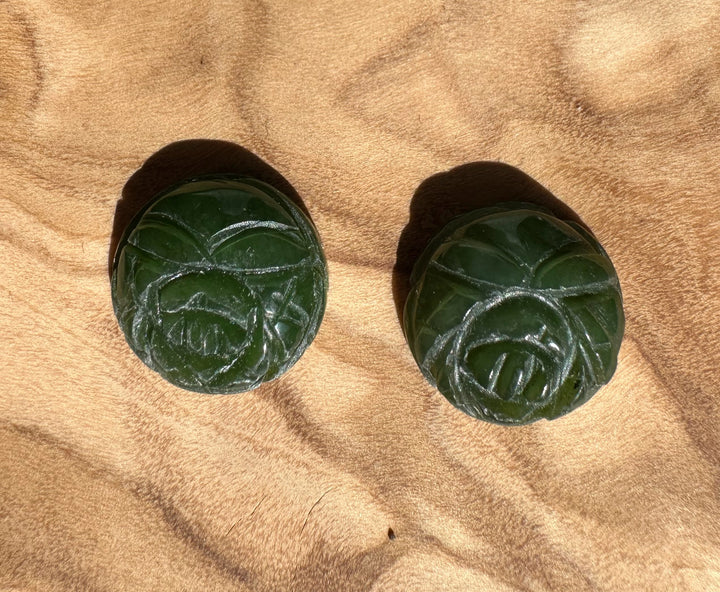 Two round dark green jade rose cabochons with carved petal designs resting on brown fabric