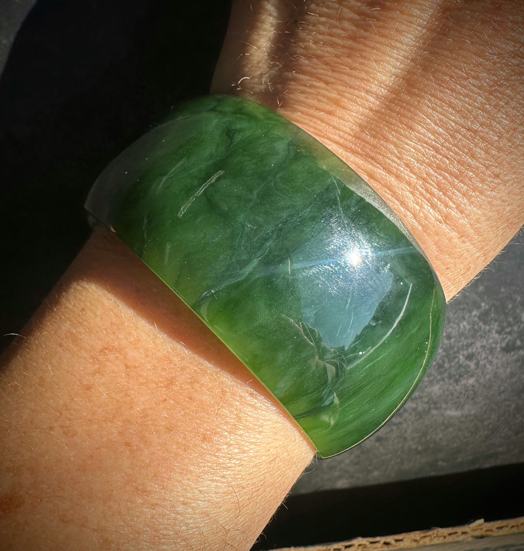 A thick, polished green jade bangle bracelet worn on a person&