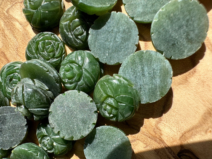 Vintage dark green jade rose cabochons and round discs scattered on a wooden surface