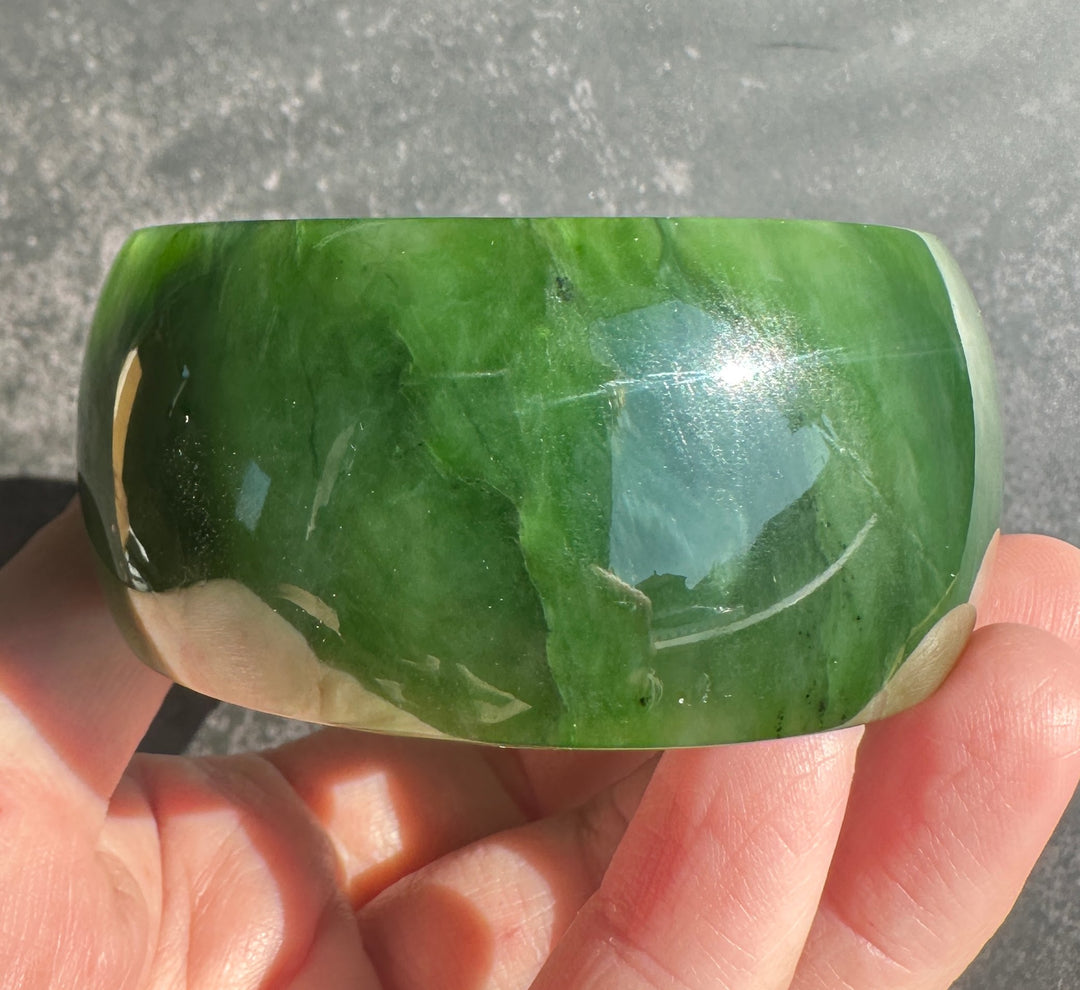 A polished green jade bangle bracelet held in a person&