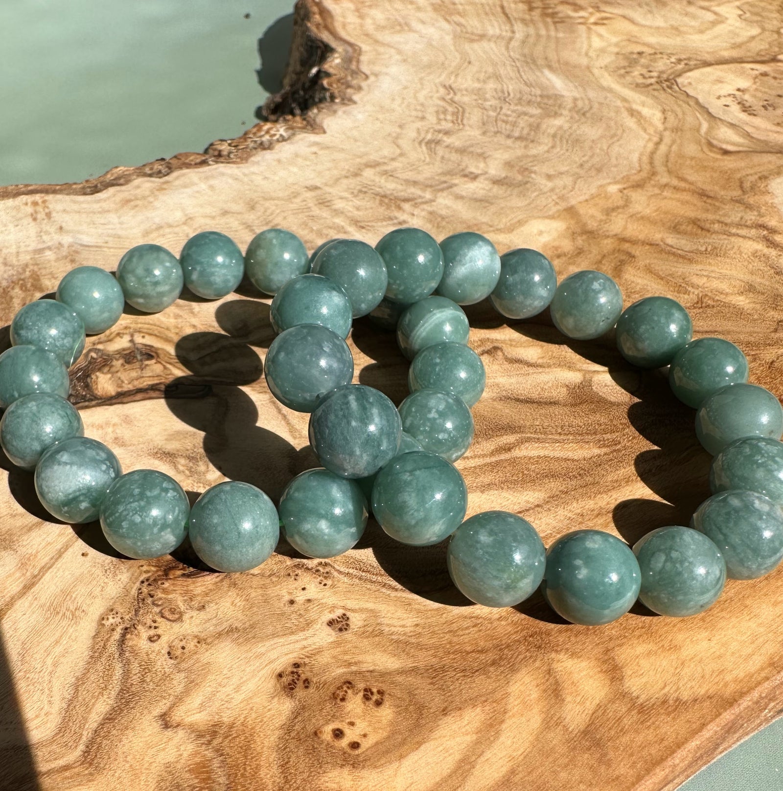 Guatemalan jadeite bead bracelet with 12mm teal-green beads resting on a textured wooden surface
