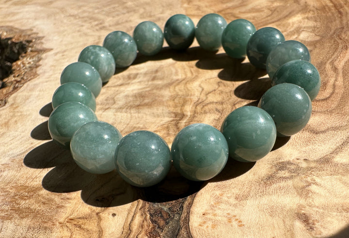 Guatemalan jadeite bead bracelet 12mm laid in a circle on a warm wood surface