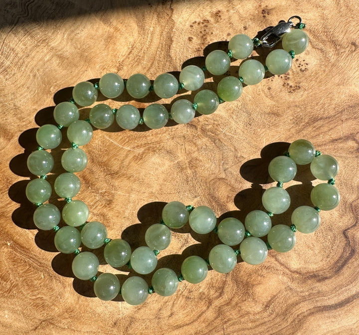 A strand of light green jade round beads with a dark metal lobster clasp, displayed on a textured wooden surface.