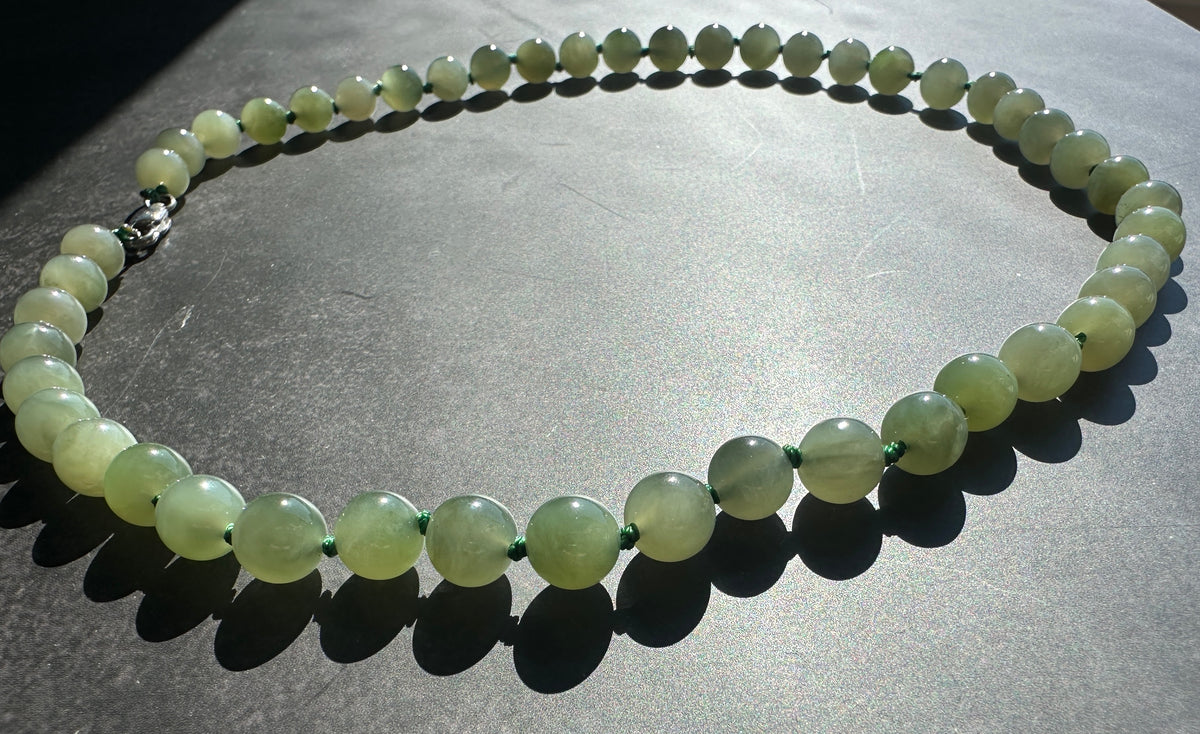 A beaded necklace made of smooth, pale green round beads with a silver-toned clasp, displayed on a dark gray surface.