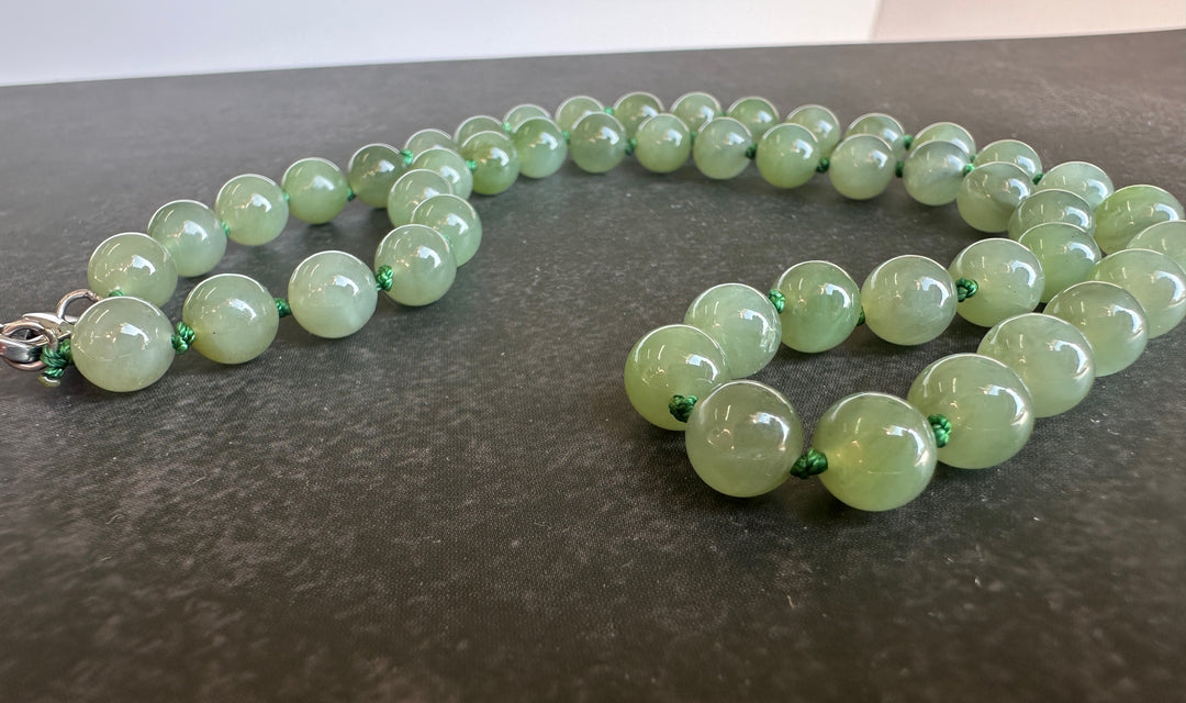 A strand of light green jade round beads with small green spacer accents and a silver clasp, displayed on a dark gray textured surface.