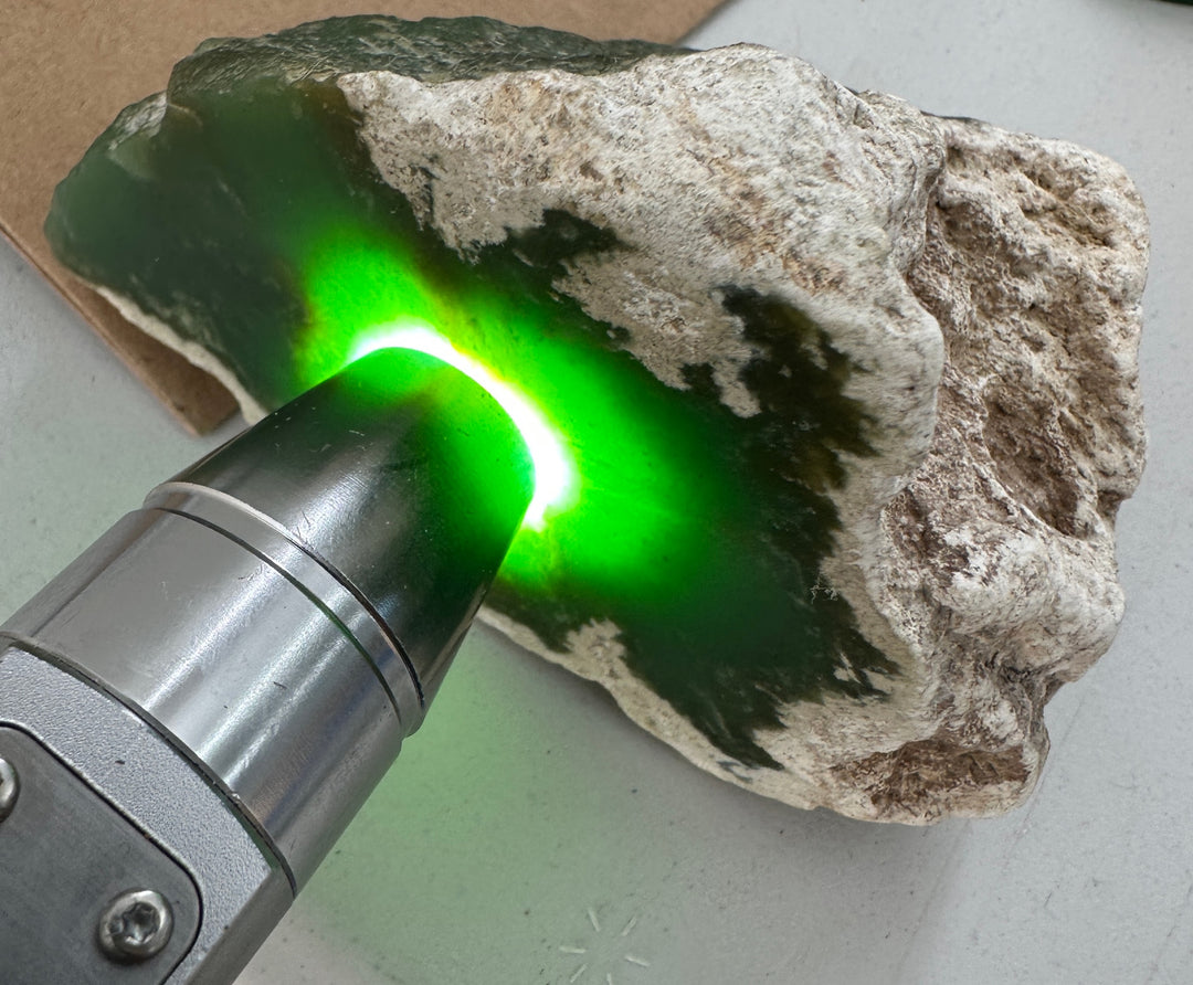 A close-up of a rough green jade bright green glow being projected onto it by a handheld metal light device.