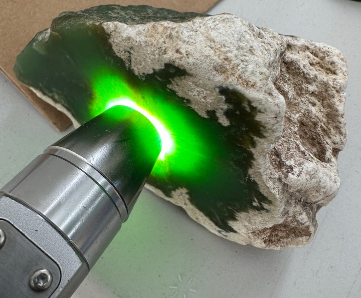 A close-up of a rough green jade bright green glow being projected onto it by a handheld metal light device.