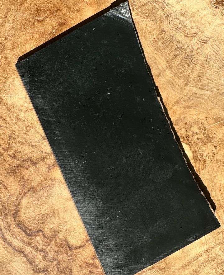 A rectangular black rough, natural edges, placed diagonally on a polished wood slice background.