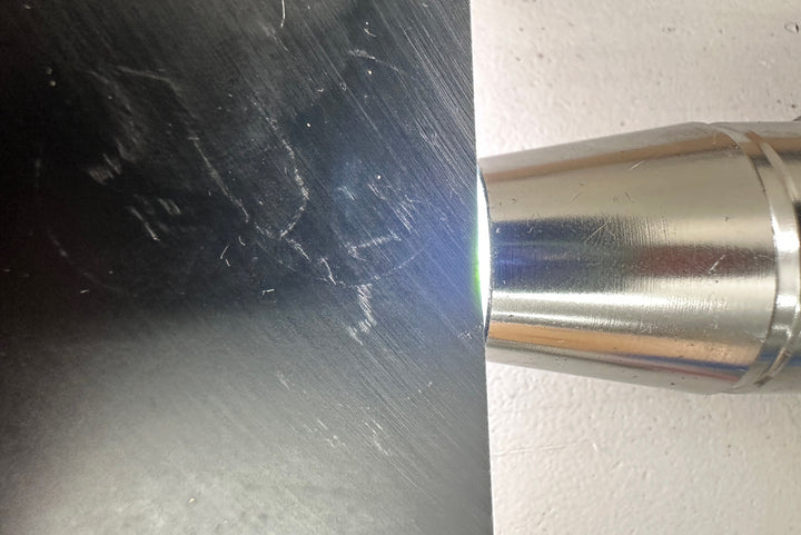 A close-up shot of jade tool or device touching a dark scratched black surface against a white background.