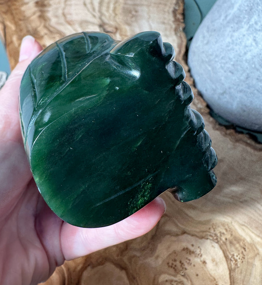 Close up of a dark green jade owl being held, showing carved feather details along the body