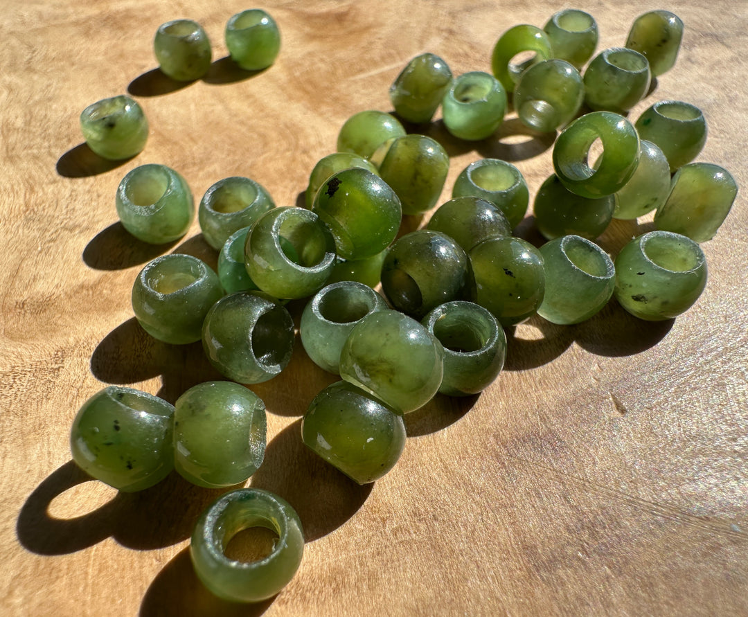 A pile of green jade beads with hollow centers, resting on a wooden surface under direct sunlight.