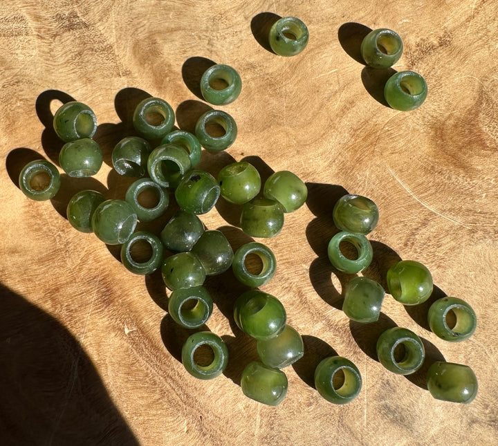 Cluster of 6mm Canadian Jade beads with large holes scattered on a wooden surface