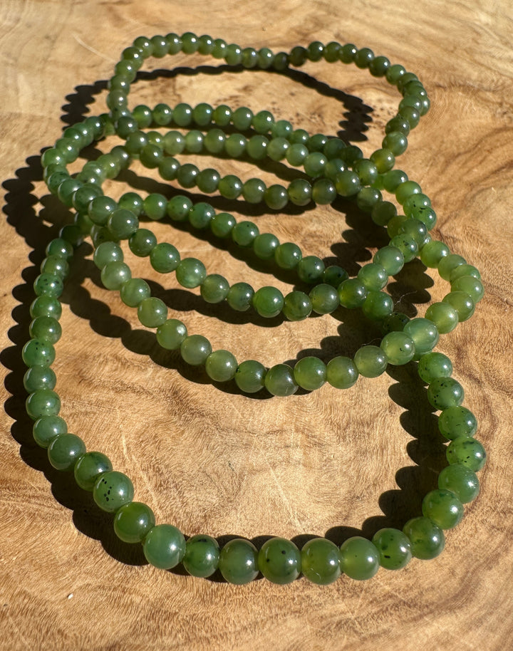 Multiple strands of green jade beaded bracelet made of polished round beads, displayed on a textured wooden surface.