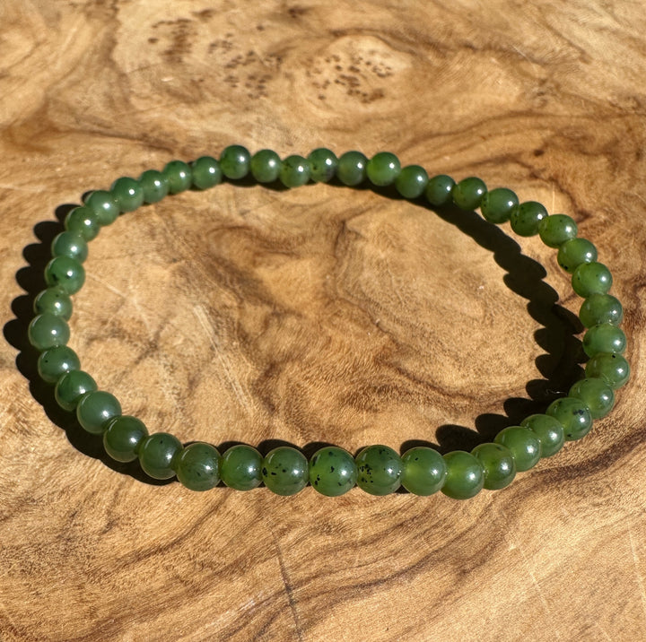A green beaded bracelet made of polished round beads, displayed on a textured wooden surface.