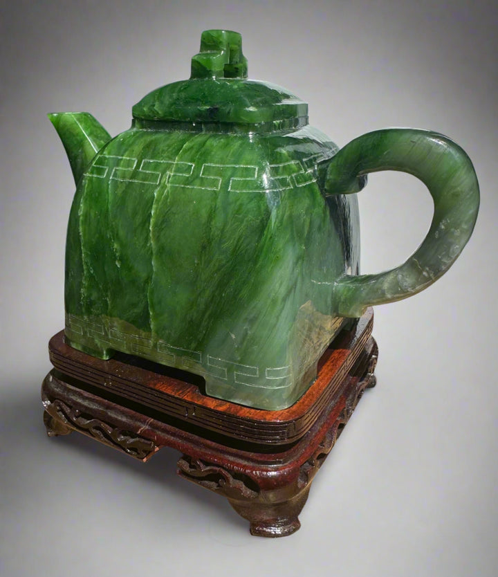 Polar Jade Teapot on a carved wooden stand with a green jade body and geometric banding around the midsection