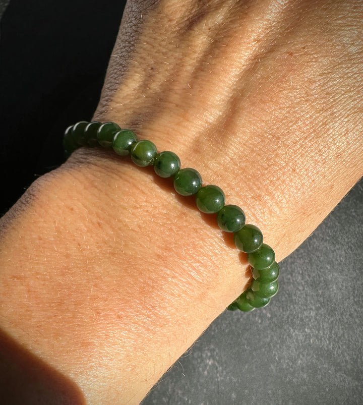 A green beaded bracelet made of polished round jade-like beads, shown worn on a person&