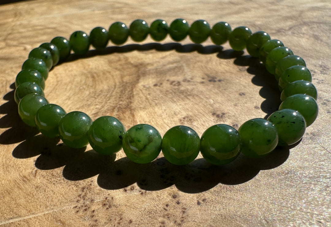 A beaded stretch bracelet made of polished green jade-like round beads, displayed on a textured wooden surface.