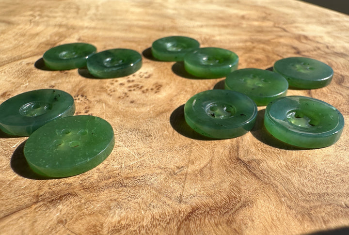 A group of translucent green buttons scattered on a textured wooden surface.