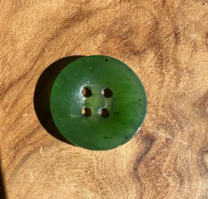 A single round green button with four holes, photographed from above on a textured brown wood surface.