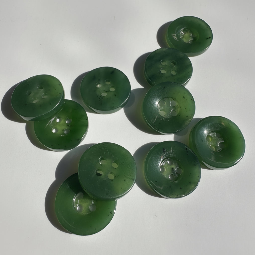 A set of ten translucent green jade buttons with four holes, arranged on a white surface with soft shadows.