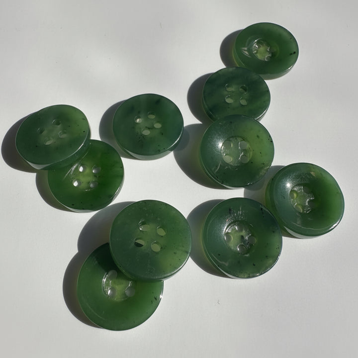 A set of ten translucent green jade buttons with four holes, arranged on a white surface with soft shadows.