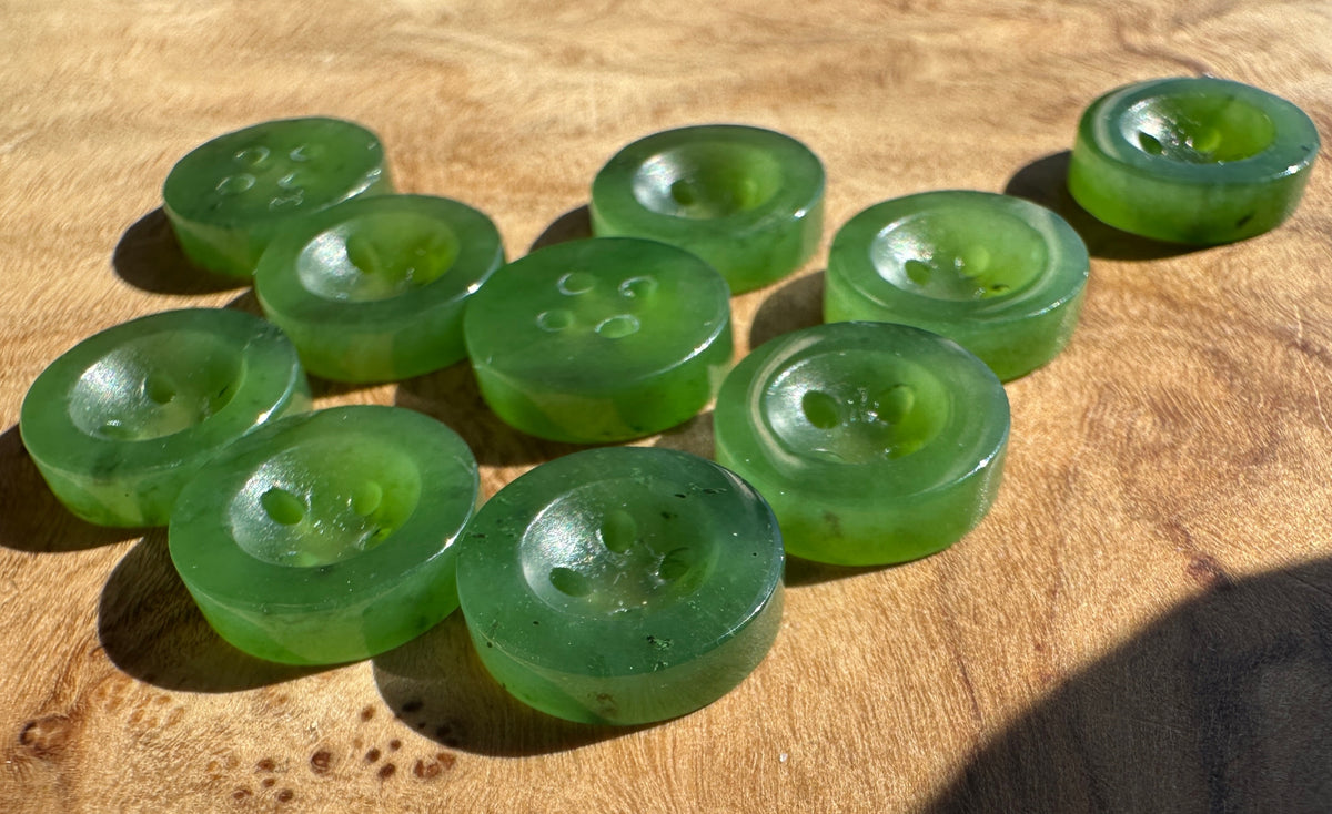 Translucent green jade buttons with varying hole counts, arranged on a wooden surface under direct sunlight.