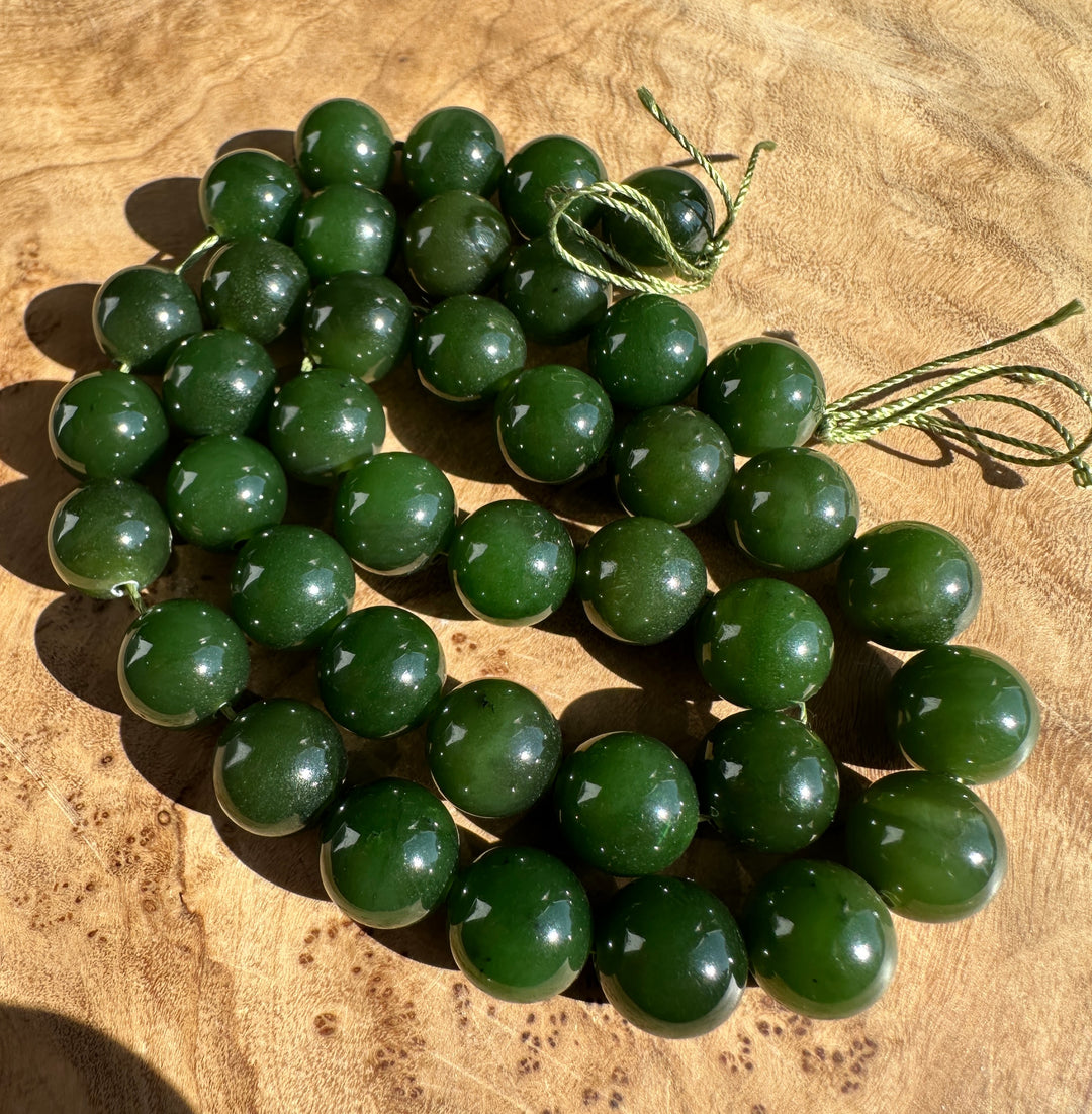 A strand of polished dark green jade beads with a matching green cord, arranged on a textured wooden surface.