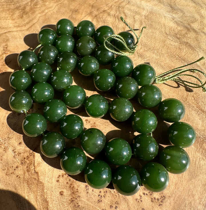 A strand of polished dark green jade beads with a matching green cord, arranged on a textured wooden surface.