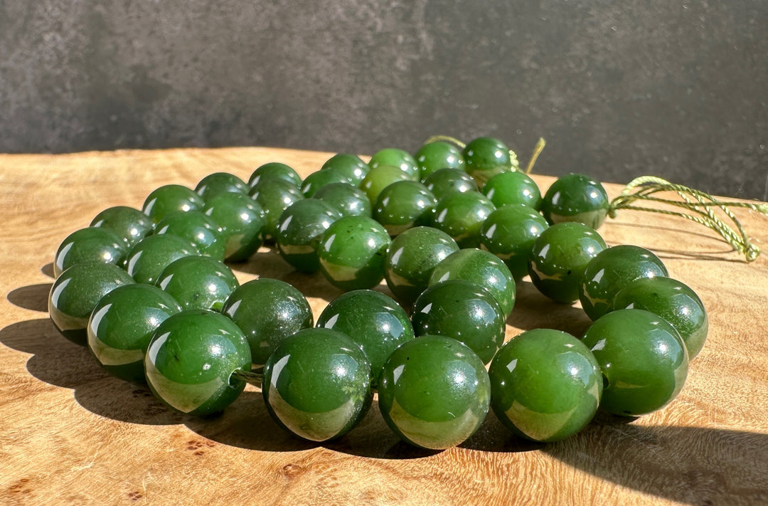 A strand of polished green jade round beads with a matching cord, arranged on a wooden surface against a dark gray background.