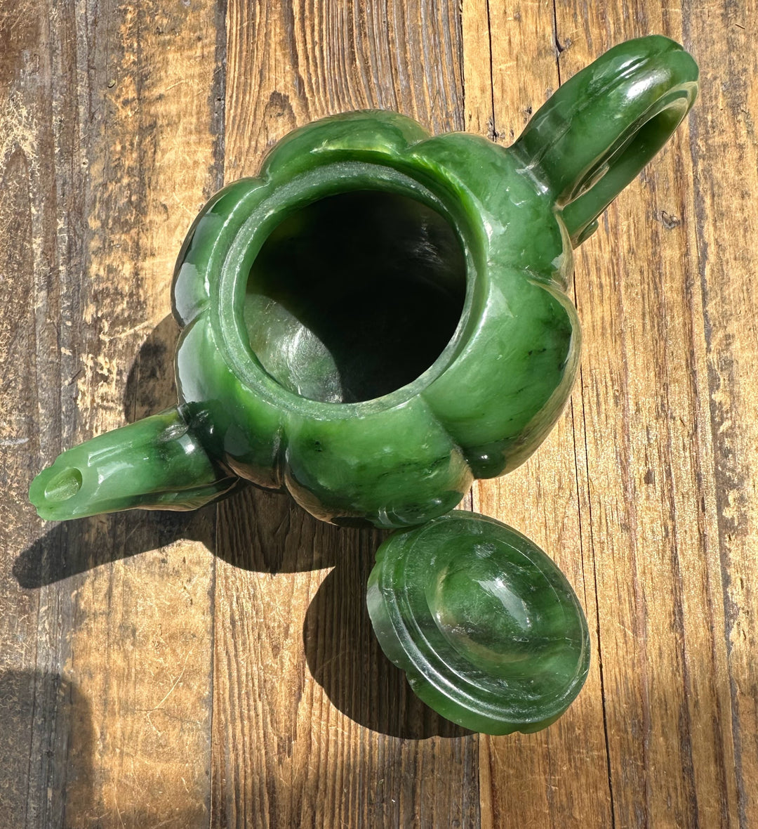 Top view of Polar Jade teapot in green jade with open mouth and detached lid beside it on a weathered wooden surface.