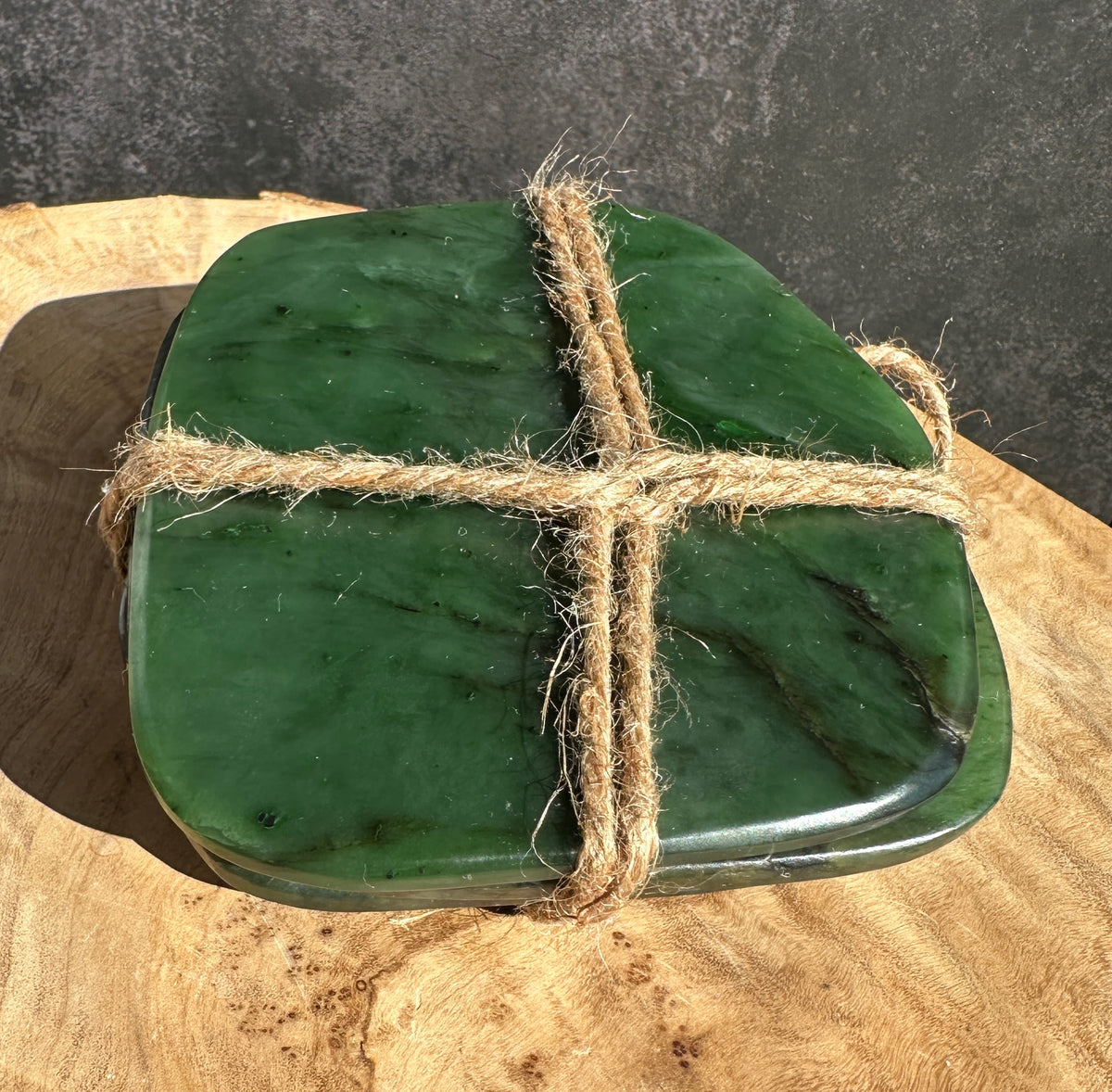 Green jade coasters tied with rustic twine , sitting on a wooden slab